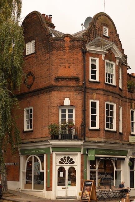 A quiet residential street in West Hampstead during daylight, featuring a narrow road with a double yellow line along the curbside. On the left, there are brick residential buildings with varying wind